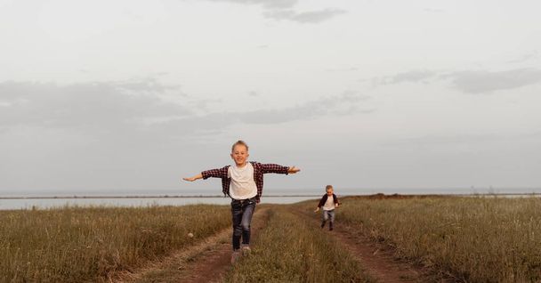 Kot pantolonlu küçük bir çocuk koşuyor, kollarını tarlanın karşısındaki izleyiciye doğru açıyor. Gökyüzü bulutlu. Seçici odaklı görüntü. metin için yer - Fotoğraf, Görsel