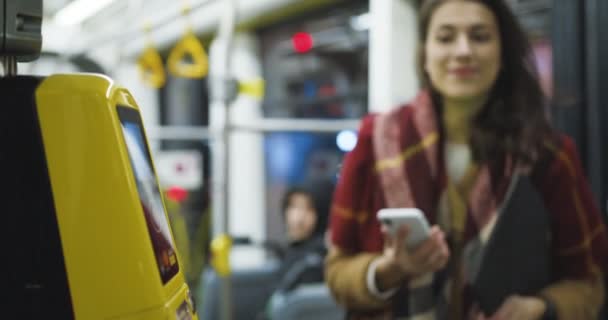 Detailní záběr žlutého bluetooth skeneru jízdenek v tramvaji nebo autobuse. Žena skenuje smartphone, aby zaplatila veřejnou dopravu. Platba po telefonu. Dívka platí za výlet. - Záběry, video
