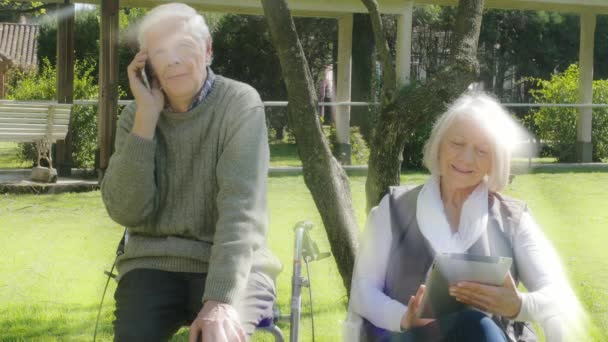 Emekli çift tabletle oynuyor ve dışarıda cep telefonuyla konuşuyor. Arkadan gelen ışık ışınları - Video, Çekim