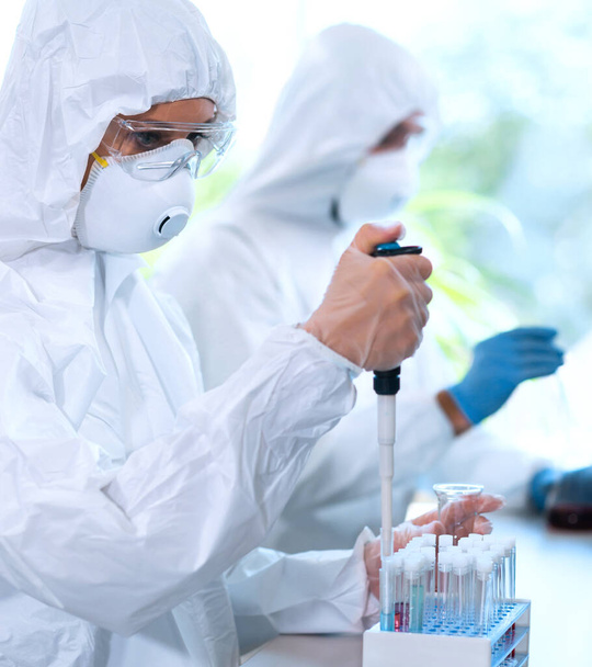 Scientists in protection suits and masks working in research lab using laboratory equipment: microscopes, test tubes. Biological hazard, pharmaceutical discovery, bacteriology and virology concept. - Foto, afbeelding
