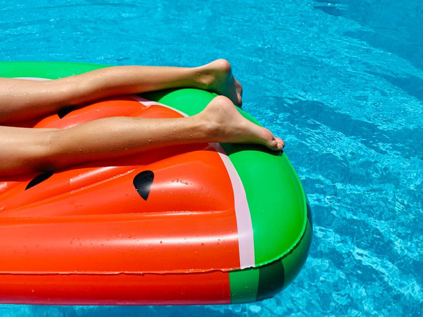 Teenaged boy floating in a swimming pool in an inflatable watermelon - Photo, image