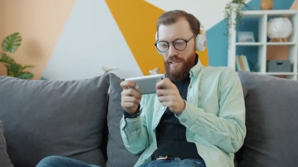 Slow motion of happy guy wearing headphones playing video game alone in studio - Кадри, відео