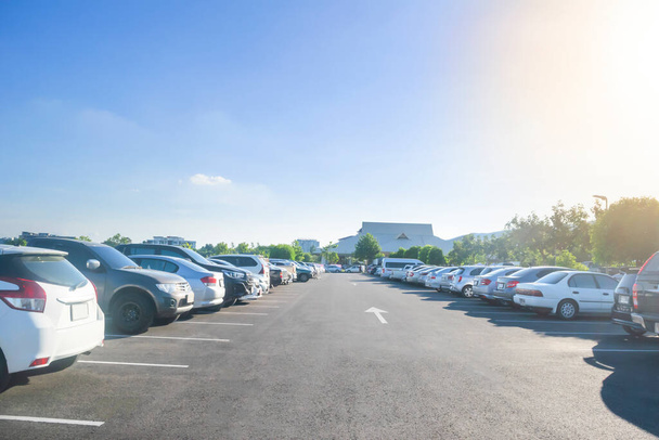 Car parking in large asphalt parking lot with trees, sunlight and blue sky background in front of hall building. Outdoor parking lot with fresh ozone and green environment concept - Photo, Image
