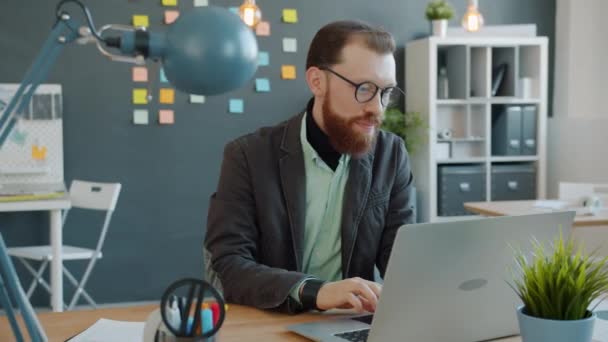 Boldog fiatalember élvezi a sikeres munkát nézi a számítógép képernyőn az irodában - Felvétel, videó