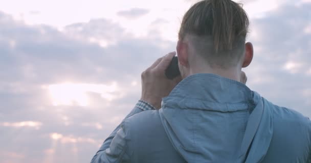 Makró hátlap portré egy stílusos férfiról, aki távcsővel nézi a horizontot a kézi eszközhöz. Közelkép a felismerhetetlen fickóról, aki megfigyeli a természetet, a mező-üveg másoló szöveggel. Férfi ruhák haj divat - Felvétel, videó