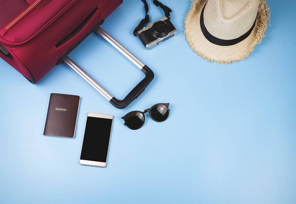 Ploché ležely cestovní doplňky, pas, klobouk, mobilní telefon, fotoaparát, sluneční brýle a růžový kufr na modrém pozadí. cestovní koncept. - Fotografie, Obrázek