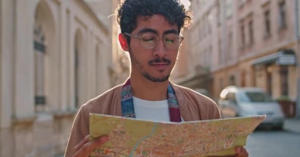 Millennial male tourist with nose ring looking at map and than at monument in front of him. Handsome guy in glasses standing at old city street. Concept of travelling and tourism. - Séquence, vidéo
