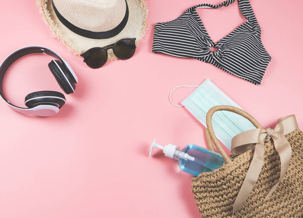 COVID-19 prevenzione, estate e nuovo concetto normale, vista dall'alto del costume da bagno bikini e accessori per le vacanze delle donne con maschera chirurgica e gel igienizzante in sacchetto tessuto su sfondo rosa. - Foto, immagini
