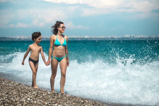 Woman with a child on the beach in Turkey, Mom and son go swimming in the sea, a boy and Mom relax on the ocean coast, beautiful sea waves. - Foto, Imagen