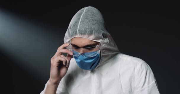 Portré kaukázusi férfi fiatal epidemiológus teljesen felszerelt jelmez védelem és orvosi maszk, hogy a szemüveg és a kamera. Veszélyes járvány. Védett orvos a covid-19 alatt. - Felvétel, videó