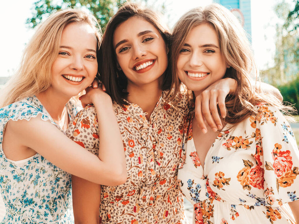 Three young beautiful smiling hipster girls in trendy summer sundress.Sexy carefree women posing on the street background. Positive models having fun and hugging.Walking after shopping - Foto, imagen