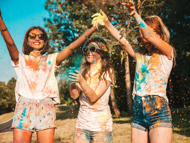 Three happy beautiful girls making party at Holi colors festival in summer time.Young smiling women friends having fun after music event at sunset.Positive models going crazy in sunglasses at sunset - Foto, afbeelding
