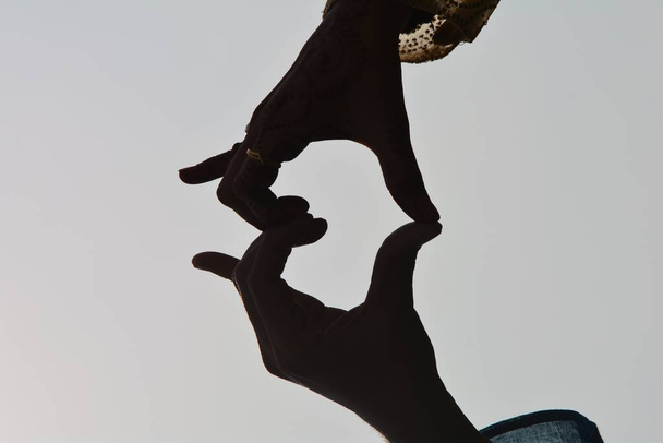 Ένας άντρας και μια γυναίκα ποζάρουν τα χέρια σαν σχήμα καρδιάς. - Φωτογραφία, εικόνα