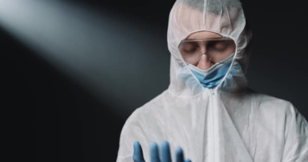 Kaukázusi férfi orvos epidemiológus teljes védőruhában és orvosi maszkban gumikesztyűt visel, mielőtt a koronavírussal dolgozna. Férfi orvos visel védelmet covid-19 vírus. - Felvétel, videó
