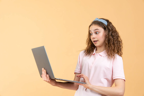 Portrét frustrovaného uživatele počítače, dospívající dívka s kudrnatými brunetkami vlasy v růžové košili při pohledu na notebook, strach z softwarové chyby, chyba programu - Fotografie, Obrázek