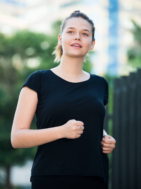 Young sporty woman running along city streets in summer morning - Foto, Bild
