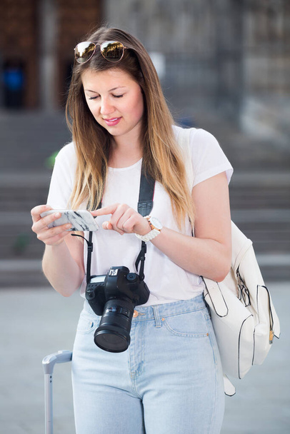 Young positive girl searching for the direction using her phone in the town - Photo, Image