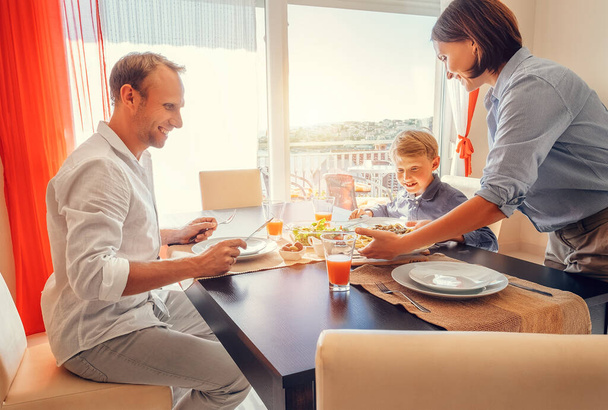 Mother brings a dish of meal at table to her hungry family - Photo, Image