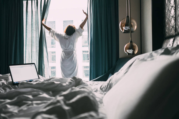 Woman stands near the window in hotel room at morning time - Foto, afbeelding