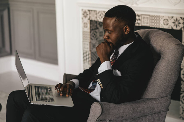 black guy in a black suit stares hard at a laptop - Fotó, kép