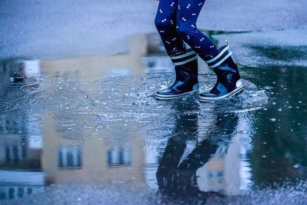 Child with rain boots jumping in puddles after rain. Childhood, laisure, happiness concept. Horizontal image - Photo, Image