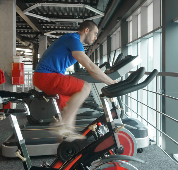 Muscular man which using spinning bicycle in gym. Bike cardio workout at the gym club. side view. - Foto, Imagen