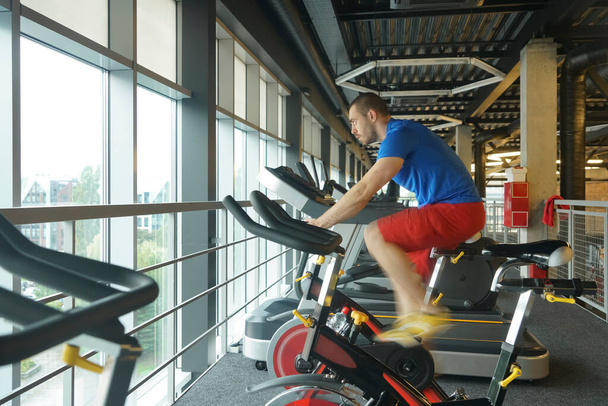 Homme musculaire qui utilise le vélo de spinning dans la salle de gym. Entraînement cardio vélo au club de gym. vue latérale. - Photo, image
