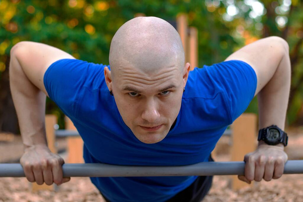Kalju mies sinisessä paidassa treenaa luonnossa vihreiden puiden ympäröimänä. - Valokuva, kuva