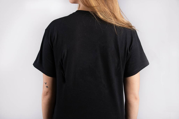 A young female wearing a black short sleeve t-shirt with a white wall in the background - Foto, Imagem