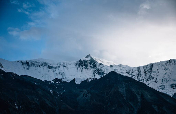 The breathtaking view of the snow-covered mountain peak captured under the clouds in the sky - Foto, afbeelding