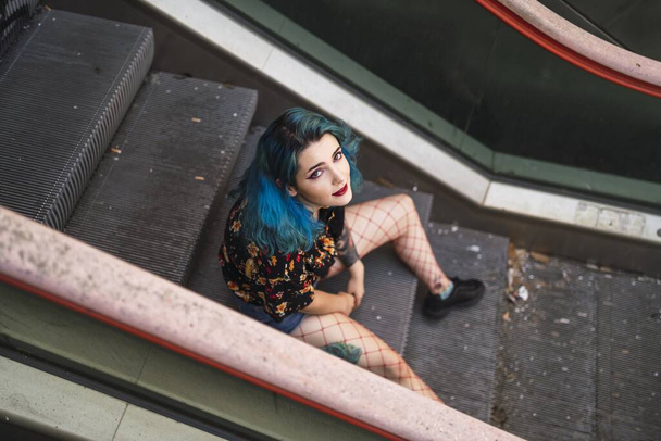 A beautiful Caucasian female with blue hair posing on an escalator in an old building - Photo, Image