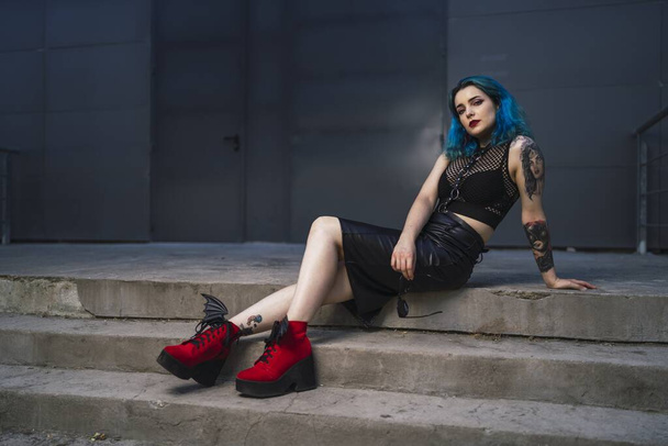 A European female with tattoo and blue hair wearing sunglasses and sexy black dress posing at the side of a building - Foto, Imagem