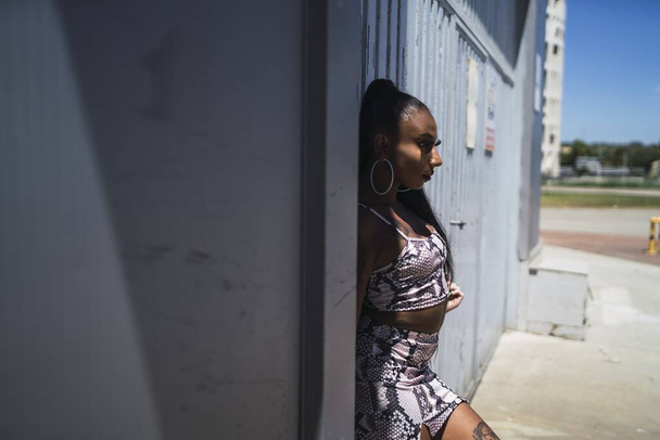 A shallow focus of a young African female leaning on a wall under the sunlight with a blurry background - Foto, imagen