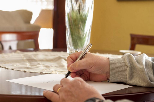 Ręce osoby starszej piszącej na białej kartce na stole - Zdjęcie, obraz