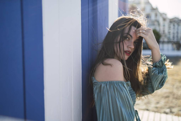A shallow focus of a young female with long hair wearing red lipstick and leaning on a wall under the sunlight - Zdjęcie, obraz