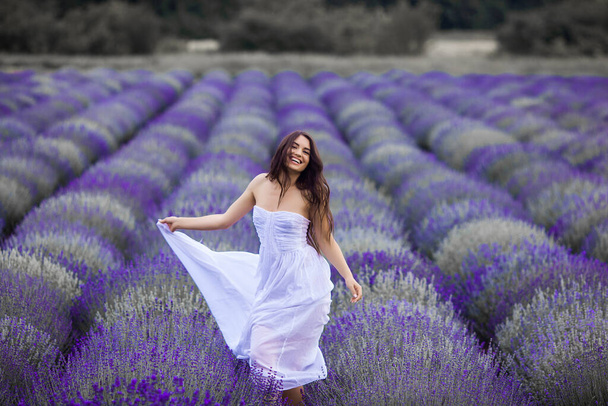 Una joven corriendo en el campo de lavanda. Hermosa mujer sobre fondo floral de verano
 - Foto, Imagen