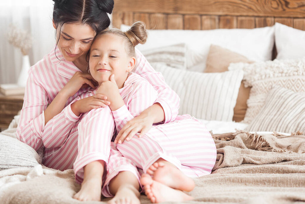 Young active mother and her little daughter having fun together at home in the bedroom wearing pajamas - Valokuva, kuva