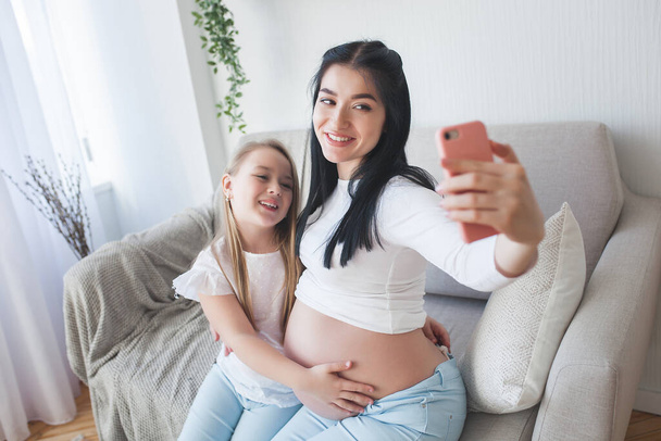 Mamma e figlioletta fanno selfie insieme. Mamma e bambino in casa a fare foto con smartphone. - Foto, immagini