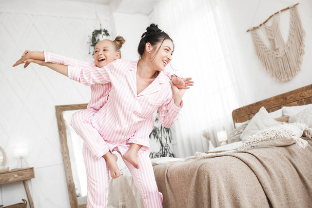 Nuori aktiivinen äiti ja hänen pieni tytär hauskaa yhdessä kotona makuuhuoneessa yllään pyjama - Valokuva, kuva