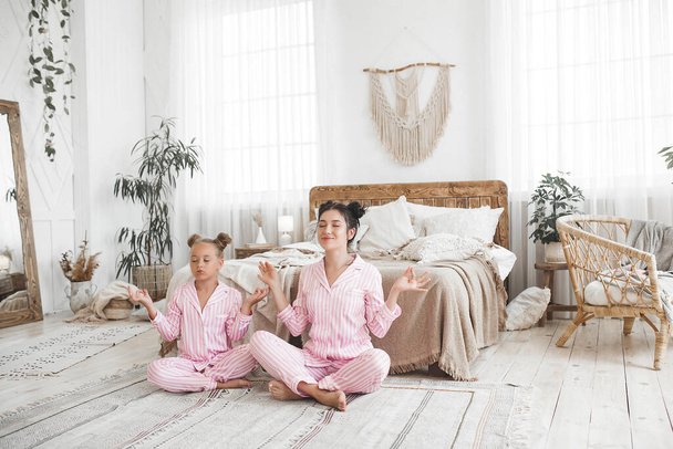 Young active mother and her little daughter having fun together at home in the bedroom wearing pajamas - Photo, Image