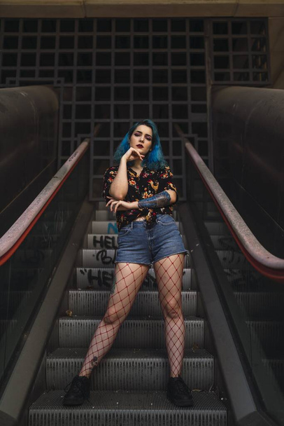 A vertical shot of a Caucasian female with blue hair posing on an escalator in an old building - Foto, immagini