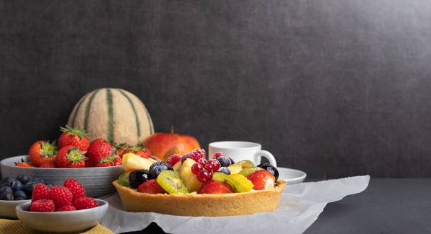 pastel de frutas casero con fresas, frambuesas, arándanos, kiwi, melón y manzana en una mesa rústica
 - Foto, imagen