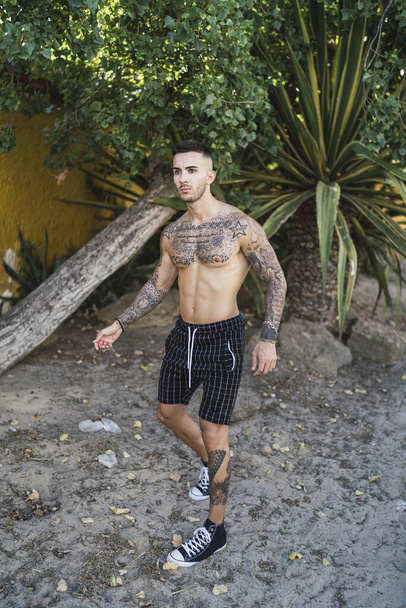 A vertical shot of Caucasian male with tattoos posing on the beach - Fotografie, Obrázek