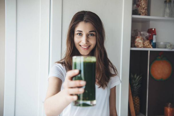 Femme brune caucasienne montrant à la caméra un jus de légumes frais pressé dans un verre et souriant - Photo, image