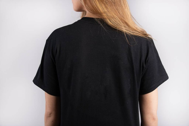A young female wearing a black short sleeve t-shirt with a white wall in the background - Valokuva, kuva