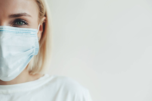 Close photo of a stunning caucasian woman with blonde hair wearing a medical mask and white t-shirt on a studio wall with free space - Zdjęcie, obraz