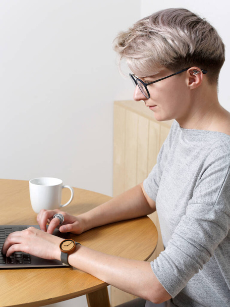 Young focused hipster millennial female with short blonde haircut working with laptop in cafe interior, close-up side view, looking at screen and typing - Фото, изображение