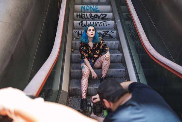 A Caucasian female with blue hair posing on an escalator and a photographer taking her picture - Fotografie, Obrázek
