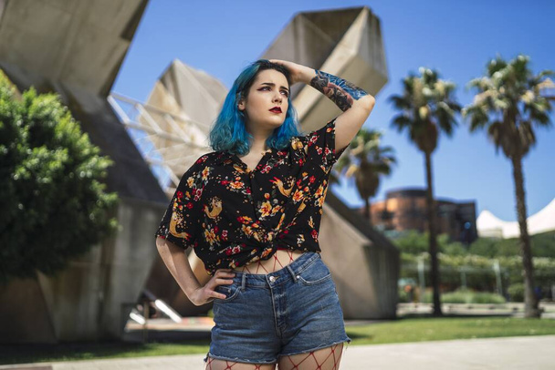 Nuori nainen, jolla on siniset hiukset shortseissa puistossa auringonvalon alla. - Valokuva, kuva