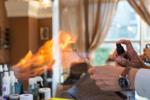 Profesjonalny męski fryzjer ogrzewa ostrze staromodnej brzytwy prostej pod strumieniem ognia dla płynniejszego golenia. Stylowy fryzjer przygotowuje narzędzia do tradycyjnego golenia brody u fryzjera - Zdjęcie, obraz